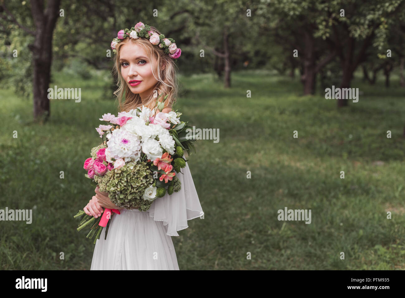 Braut in Blumen Kranz und Hochzeit Kleid mit Blumenstrauß und Kamera im Freien Stockfoto