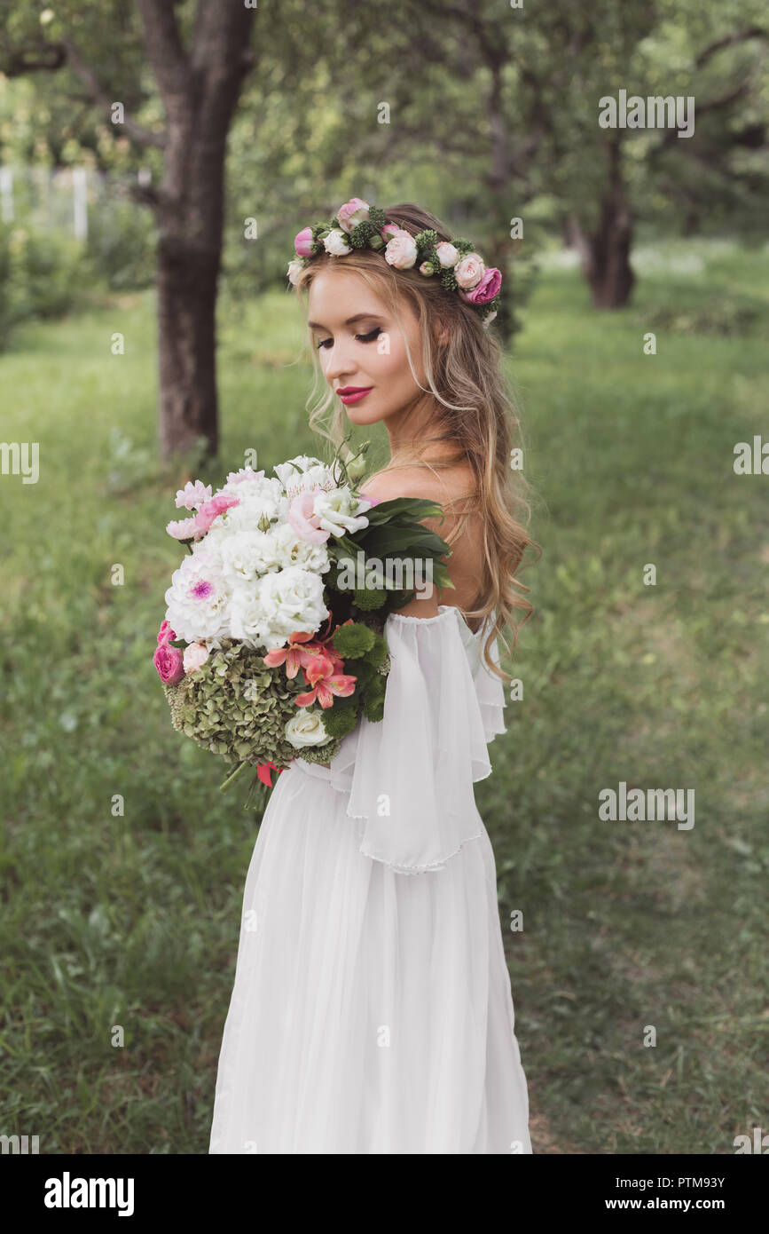 Ausschreibung junge Braut in Blumen Kranz und Wedding Dress holding Blumenstrauß im Freien Stockfoto