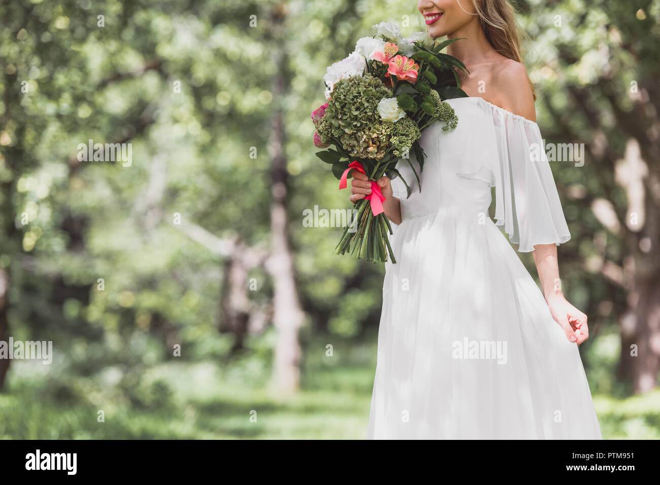 7/8 Schuß von lächelnden jungen Braut im Brautkleid holding Blumenstrauß im Freien Stockfoto