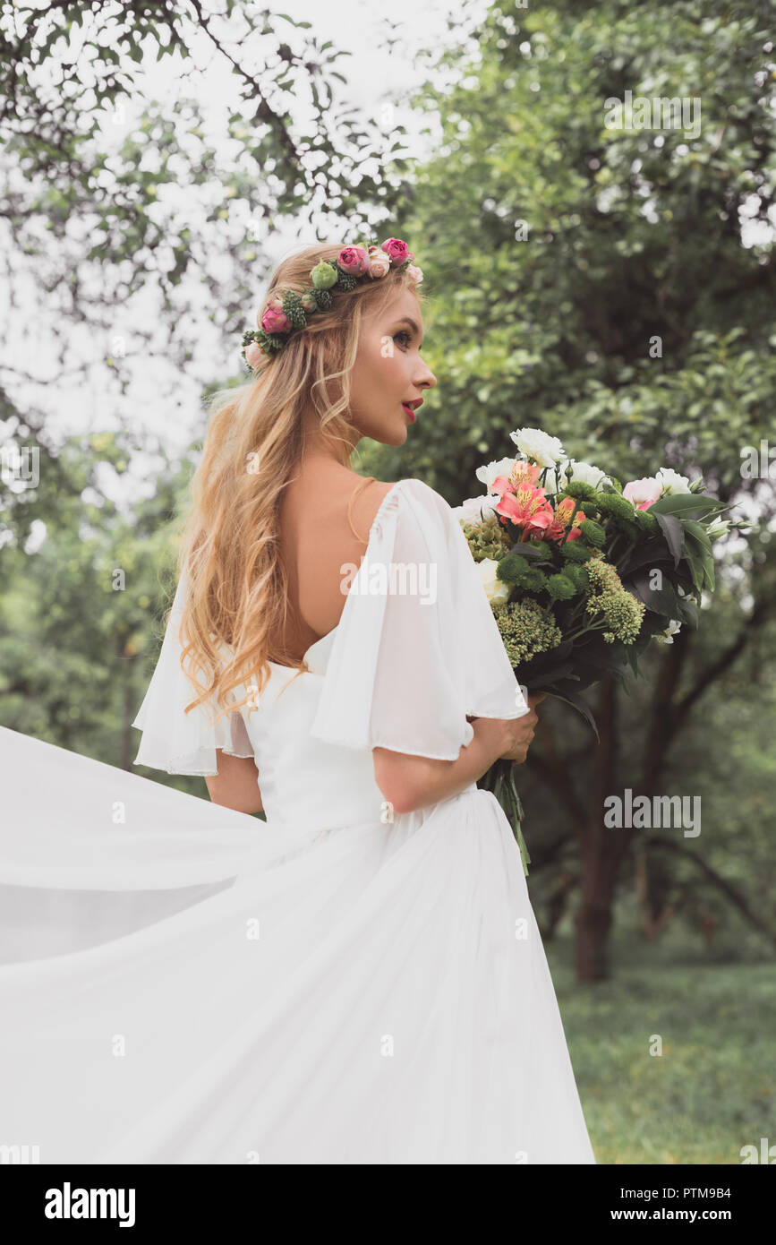 Schönen blonden Braut im Brautkleid und floralen Kranz holding Strauß Blumen im Park Stockfoto