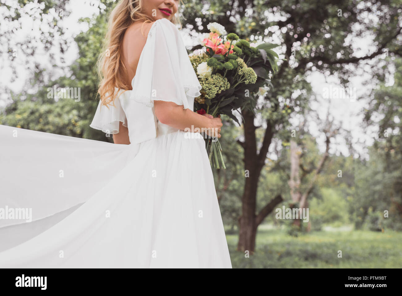 7/8 shot der jungen Braut im Brautkleid holding Blumenstrauß im Freien Stockfoto