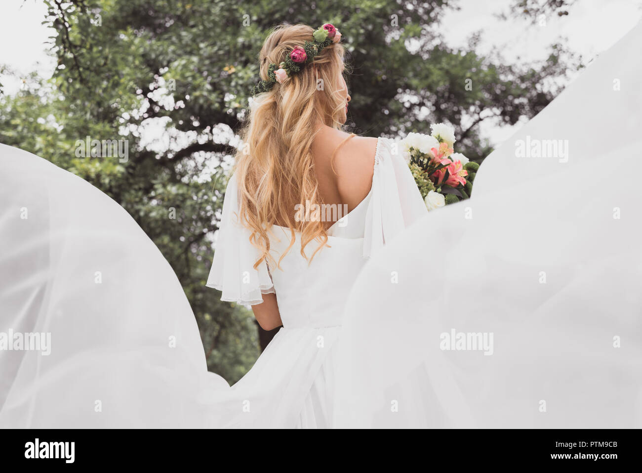 Rückansicht der blonde junge Braut im Brautkleid holding Blumenstrauß im Freien Stockfoto