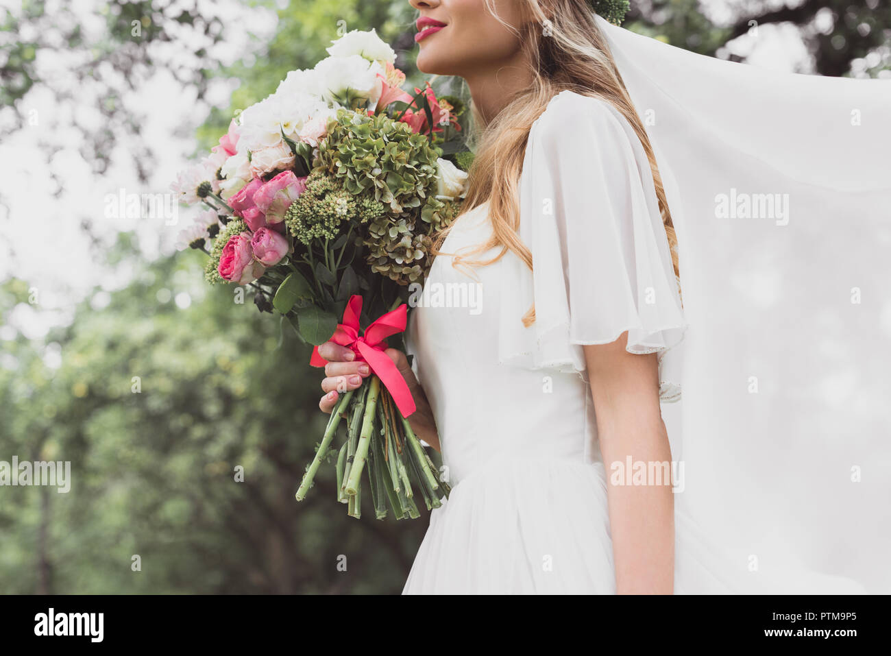 7/8 shot der jungen Braut im Brautkleid und Schleier holding Schönen Blumenstrauß Stockfoto