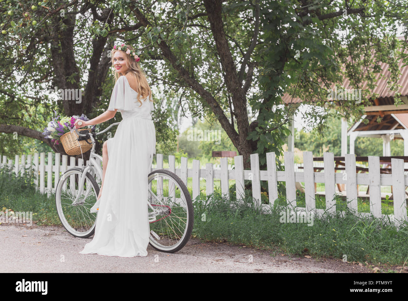 Schöne junge Braut im Brautkleid Reiten Fahrrad- und lächelnd an Kamera Stockfoto