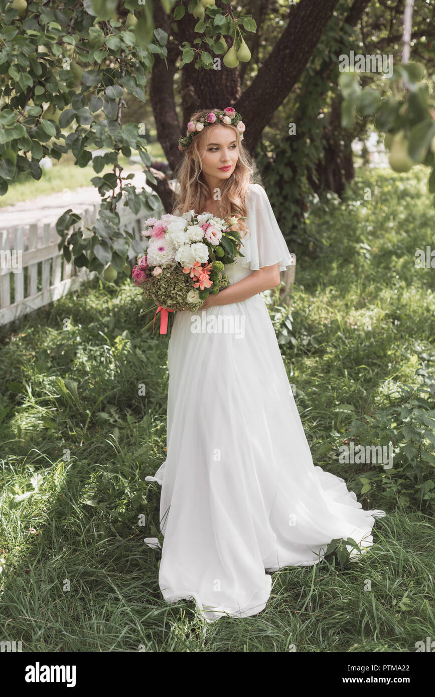 Schönen blonden Braut im Brautkleid und floralen Kranz holding Blumenstrauß und weg schauen Stockfoto