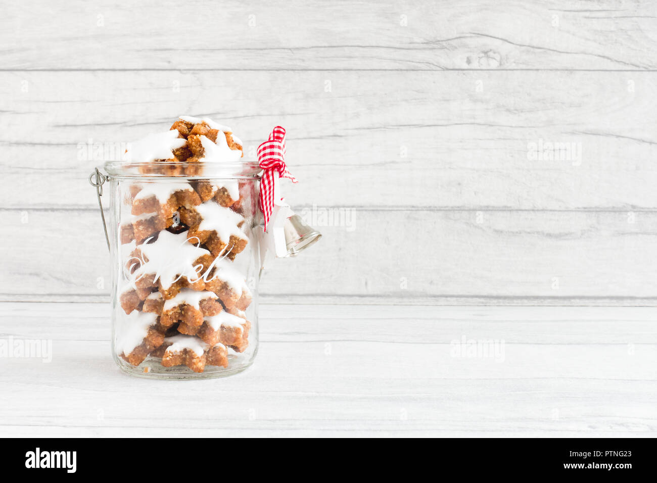 Weihnachtsplätzchen in einem Glas mit Noel schreiben, einen Bogen, silbernen Glocken und einem weißen Holz- Stern auf grau Holz Hintergrund der Kontrollleiste. Stockfoto
