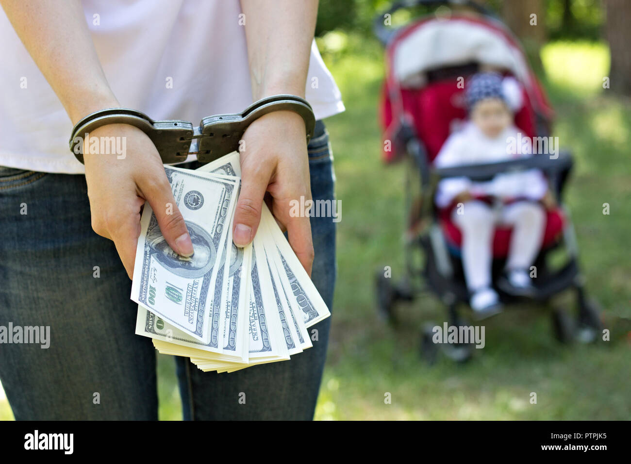 Ein Mädchen hält Geld Dollar in Handschellen vor dem Hintergrund eines Babys in eine Kutsche, Festnahme, Inhaftierung für den Verkauf von Kindern, Kinderhandel, Nahaufnahme Stockfoto