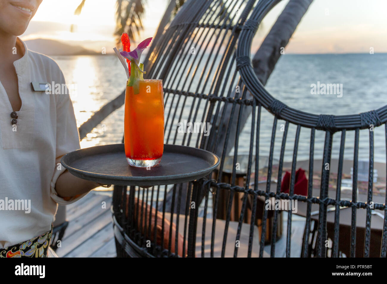 Kellner serviert Glas Cocktail am Strand bei Sonnenuntergang Stockfoto