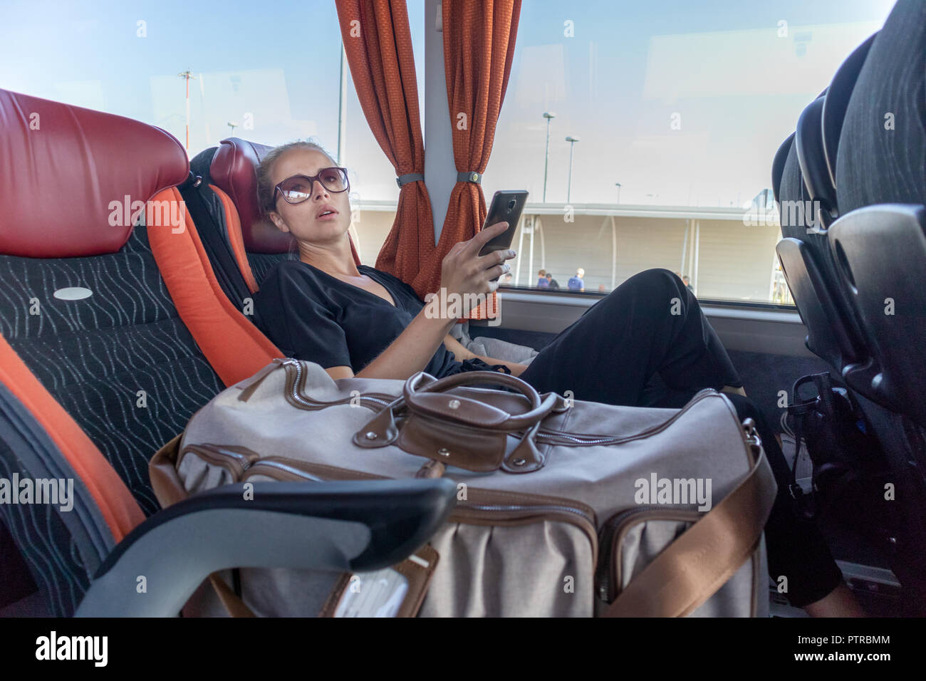 Porträt der Frau, die auf beweglichen Bus sitzen durch Fenster. Weibliche Passagier mit Smart Phone auf langen Landschaft Busfahrt nach Hause. Stockfoto