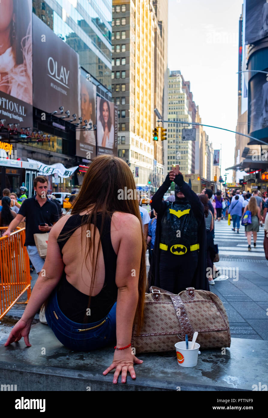 Eine junge Touristenin dreht den Spieß gegen einen Typ, der als Batman verkleidet ist, indem sie ihn in Midtown, New York, fotografieren lässt Stockfoto