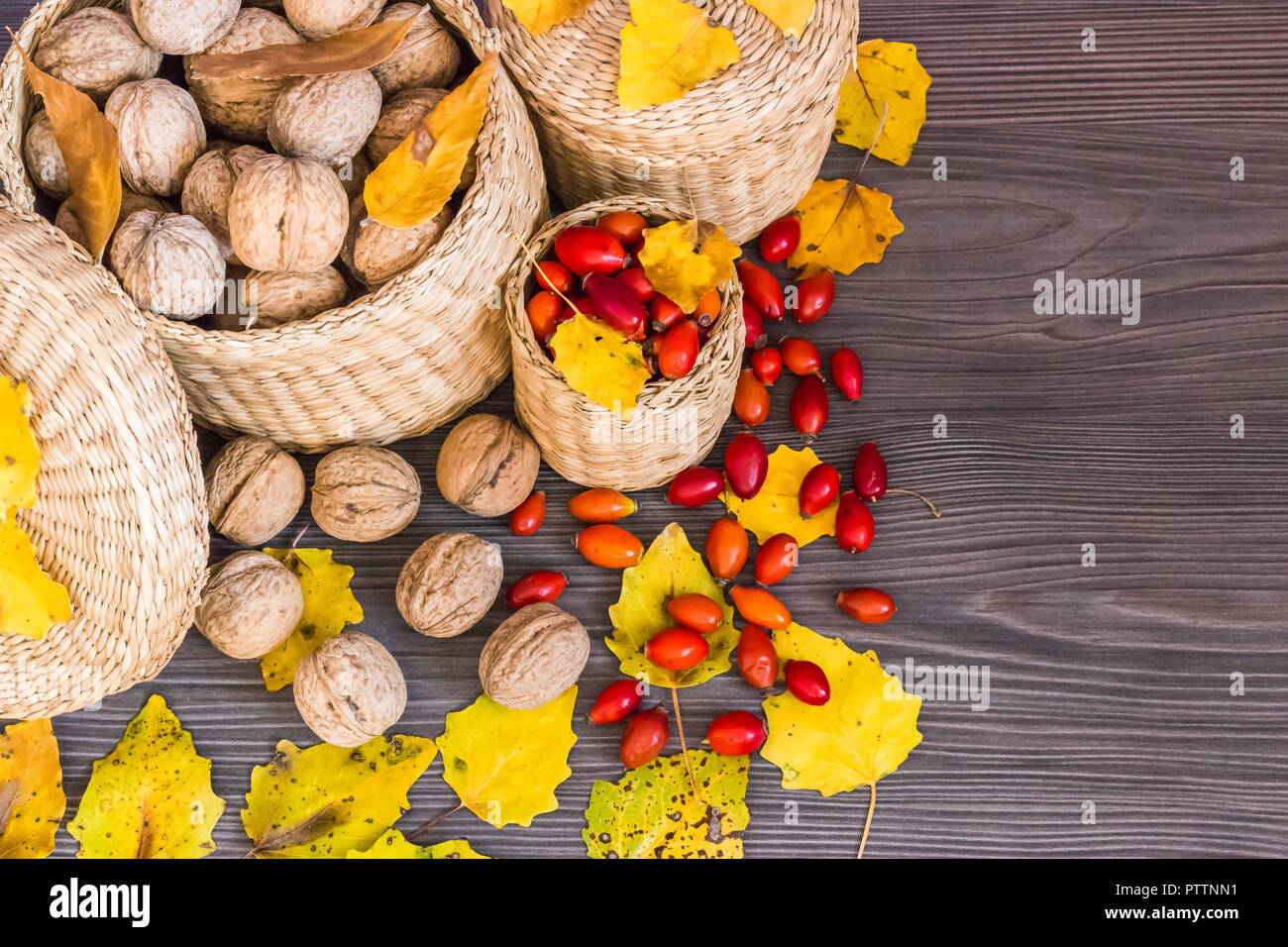 Walnüsse, Hagebutten und gelbe Blätter auf einer hölzernen Oberfläche, gesunde Nahrung aus der Natur. Konzept der Herbst Hintergrund Stockfoto