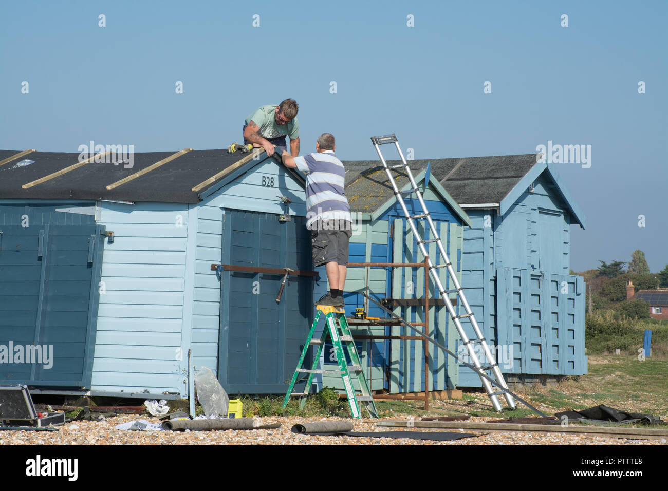 Zwei Männer arbeiten, Reparaturen auf dem Dach einer Strandhütte Stockfoto