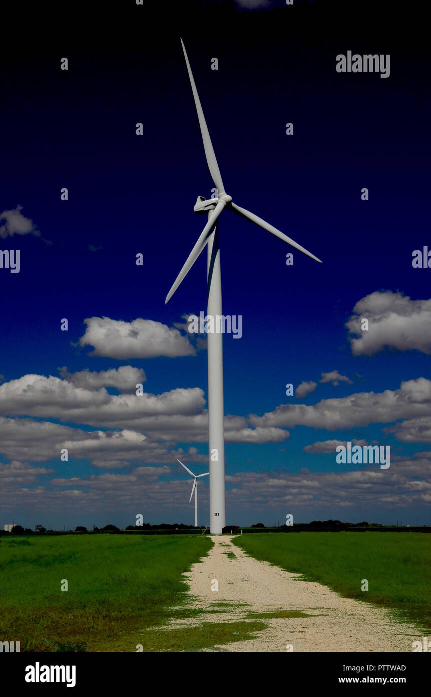 Ein Kies weg führt zu einer hohen windenergieanlage vor einem abgestuften blauer Himmel mit Wolken unter der Propeller und Kopf sichtbar gefüllt. Stockfoto