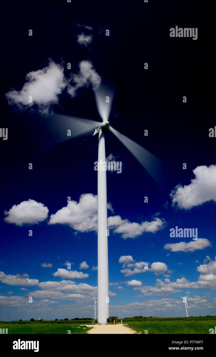 Die Rotorblätter einer Windenergieanlage blur in Bewegung gegen einen kobaltblauen Himmel und Wolken Stockfoto