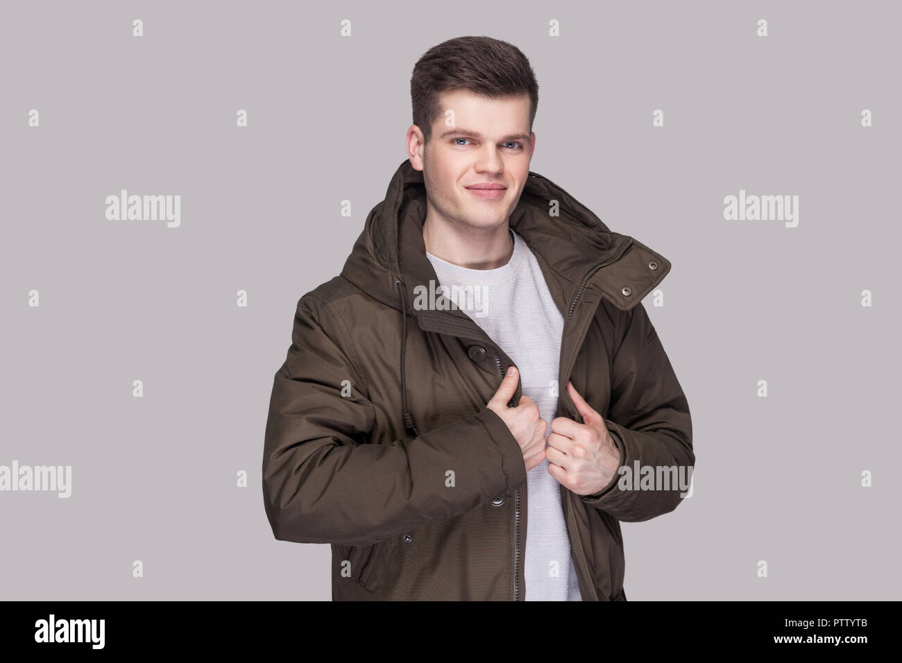 Porträt der jungen gutaussehenden Mann in Hellgrau Shirt und dunkelgrüne Parka an Kamera mit Lächeln und zufriedene Gesicht. indoor Studio shot, Stockfoto