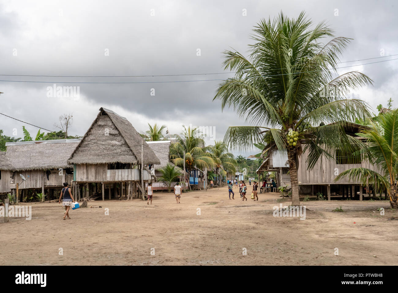 Puerto Miguel Peru, Südamerika. Native Menschen zu Fuß neben ihren Häusern auf Stelzen gebaut, neben einer Kokospalme in Puerto Miguel. Stockfoto