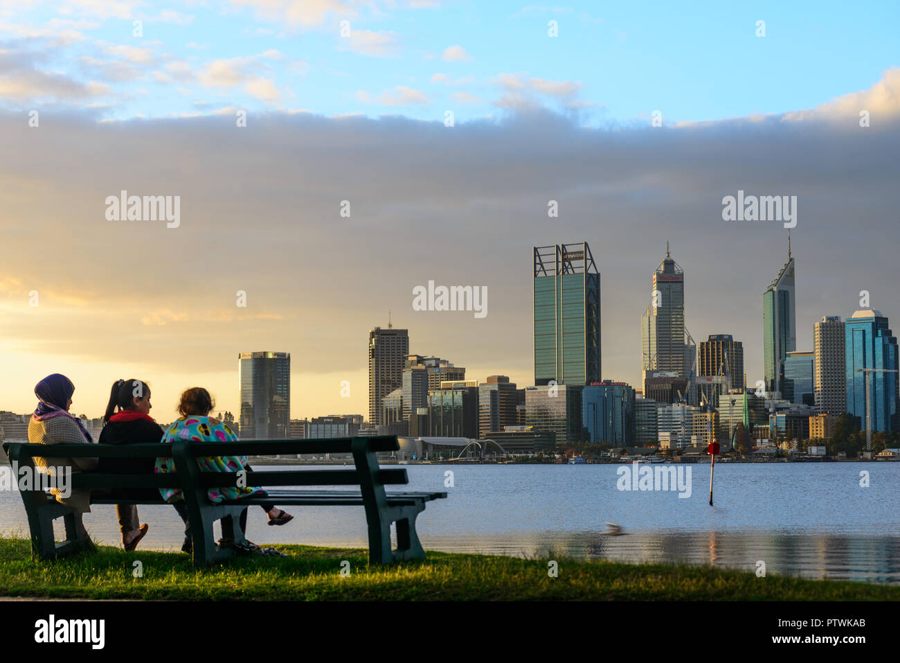 3 Personen auf einer Bank vor der Skyline von Perth mit Swan River. Ansicht von Süden Perth, Perth, Western Australia Stockfoto
