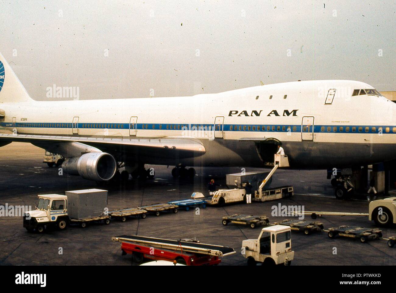Portrait der "Clipper Victor", ein Pan American World Airways 747 Jet Flugzeug am Terminal Gate am Flughafen Heathrow geparkt, außerhalb von London, England, November, 1973. Gepäckabfertigung warten mit ihren Leerlauf Gepäckträger Lkw unter dem Flugzeug öffnen Laderaum Tür. Diese bestimmten Luftfahrzeug, einem Boening 747-121 mit der Registrierungsnummer N 736 PA, hat eine berüchtigte doppelte Auszeichnung: Er bedient den Eröffnungs-Pan Am kommerziellen 747 Jet Flug am 22. Januar 1970, und sieben Jahre später wurde im Flughafen Teneriffa Disaster" vom 27. März 1977, die tödlichste Unfall in der Geschichte der Luftfahrt zerstört Stockfoto
