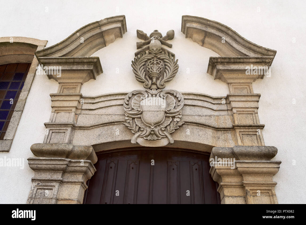 Detail der seitliche Portal mit einem gebrochenen Giebel und religiösen Wappen der barocken Kirche der Barmherzigkeit in der historischen Stadt Trancoso, Portug Stockfoto