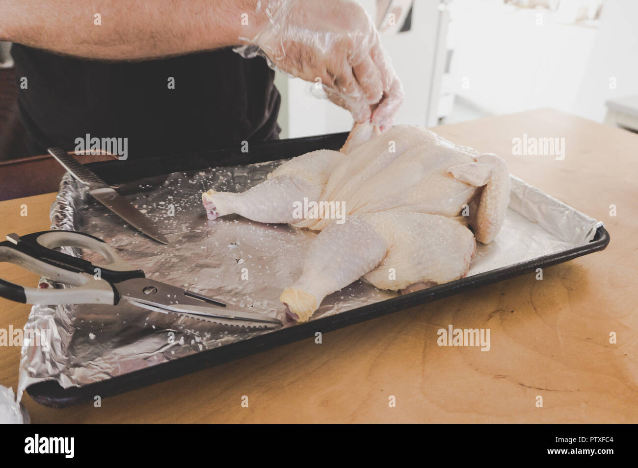 Ganze rohe Huhn, spatchcocked in Vorbereitung auf die Röstung: Hände schließen sich das Tragen der Umgang mit Lebensmitteln und Handschuhe mit Messer und Schere Stockfoto