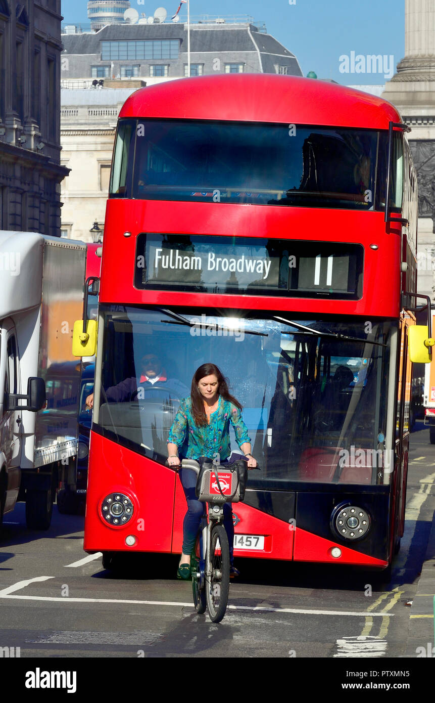 Frau Radfahren vor einem roten London Bus in Whitehall, London, England, UK. Stockfoto