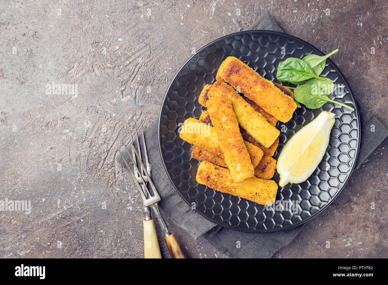 Leckere herzhafte Snacks, panierte Fischstäbchen sticks serviert auf einem Teller mit Zitrone über dunklen Stein Hintergrund, Ansicht von oben mit der Kopie Raum Stockfoto
