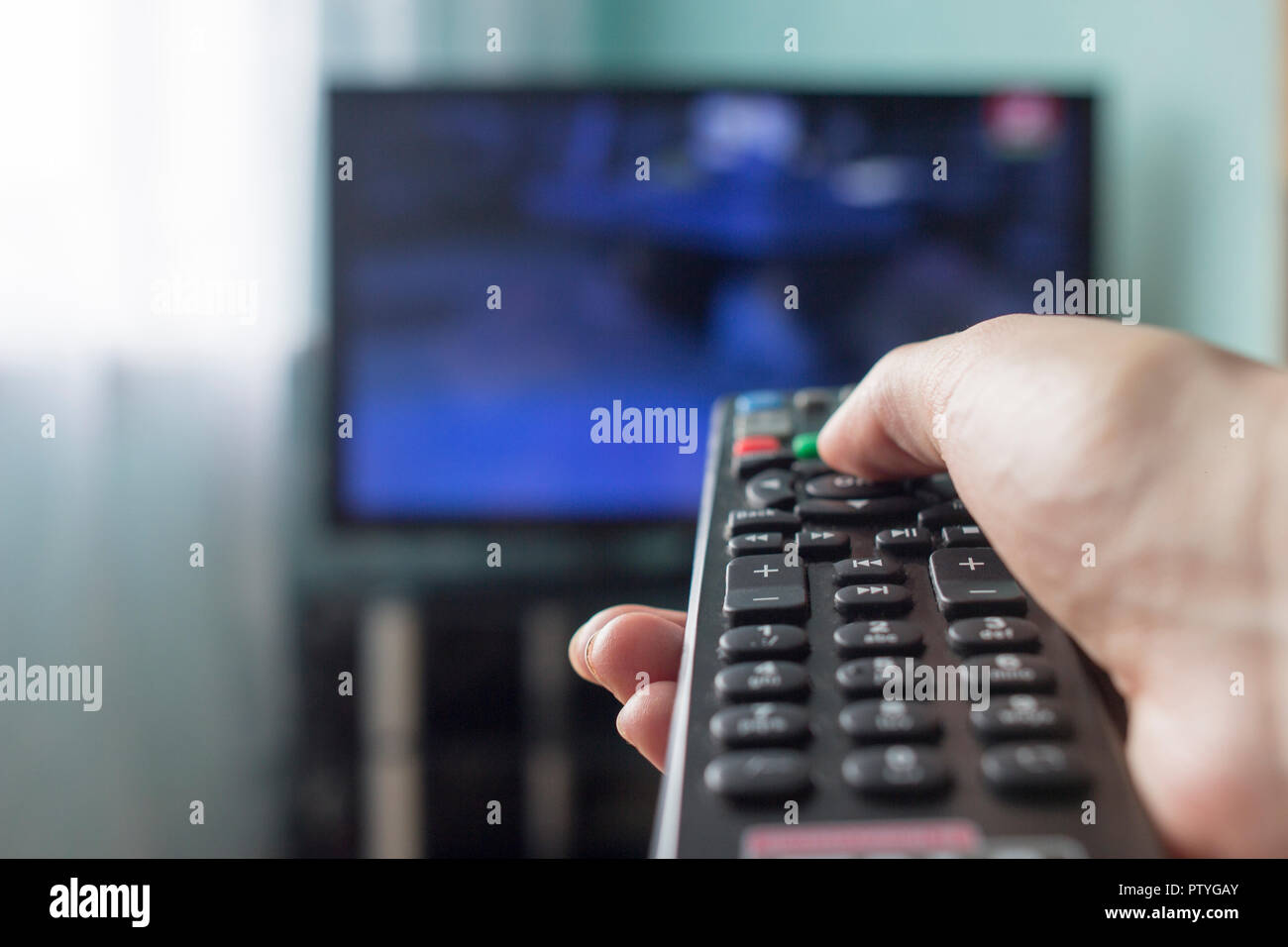 Eine Hand mit einer Fernbedienung vom TV, im Hintergrund gibt es einen TV Stockfoto