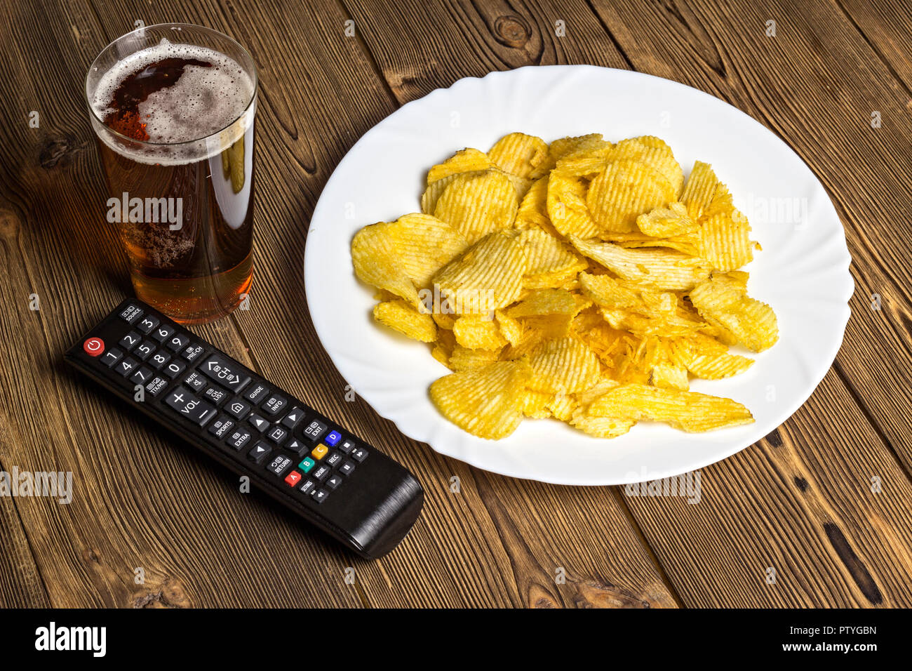 Chips mit Bier und TV-Fernbedienung auf einem hölzernen Hintergrund Stockfoto