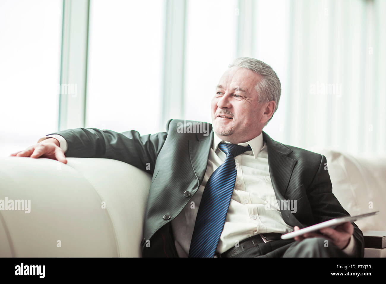 Erfolgreicher Geschäftsmann mit digitalen Tablet auf dem Sofa sitzen im eigenen Büro Stockfoto