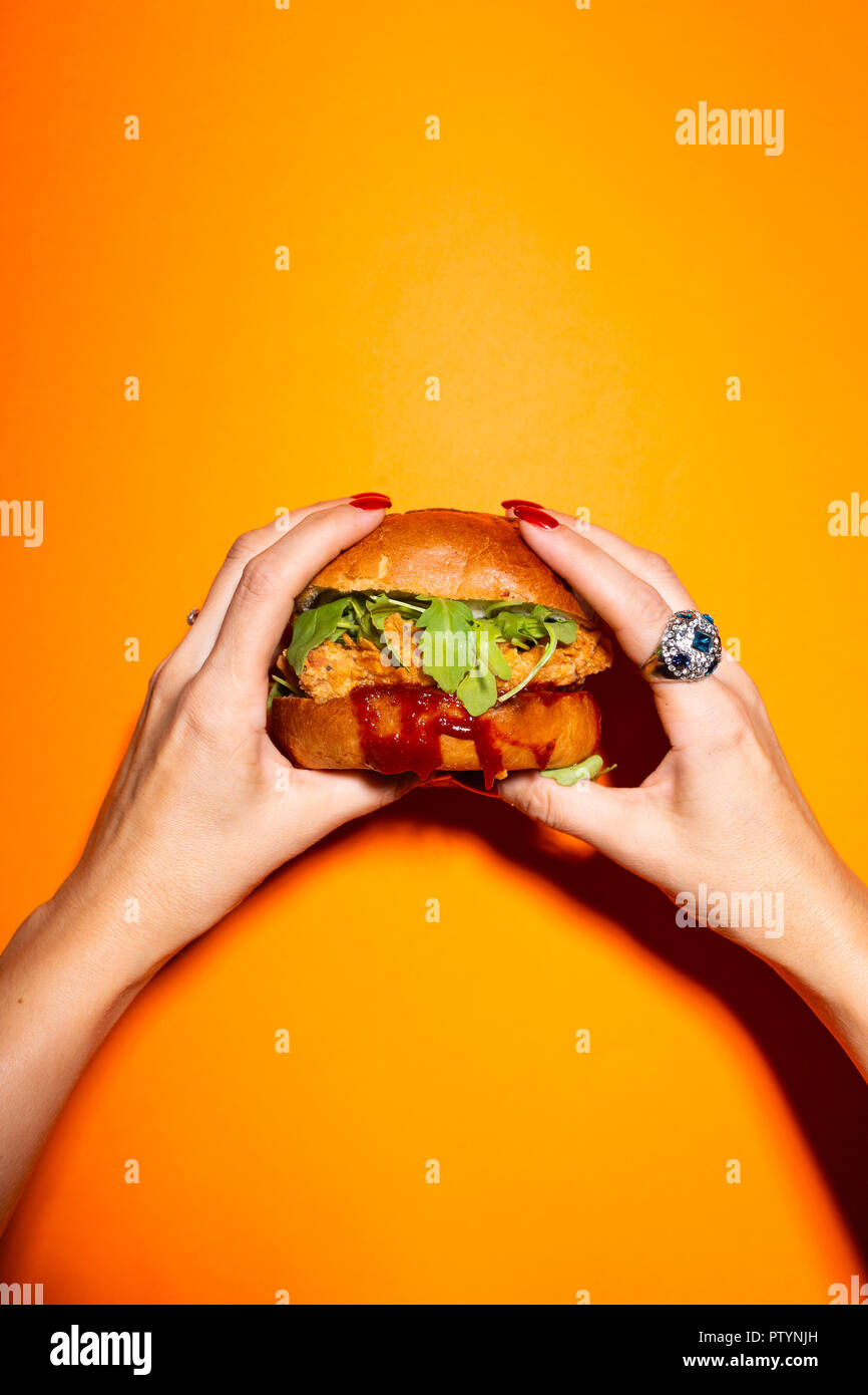 Weibliche hand Chicken Burger gegen orange hinterlegt. Stockfoto