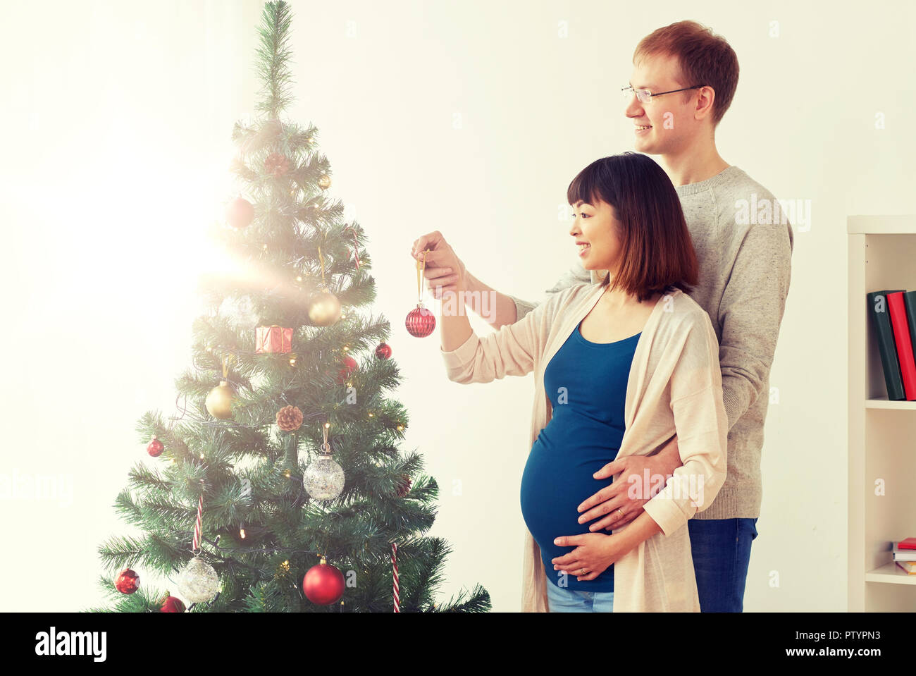 Gerne schwangere Ehefrau und Ehemann an Weihnachtsbaum Stockfoto