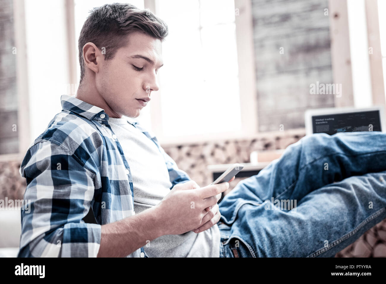Ruhiger junger Mann sitzt mit seinen Füßen und auf dem Smartphone Stockfoto