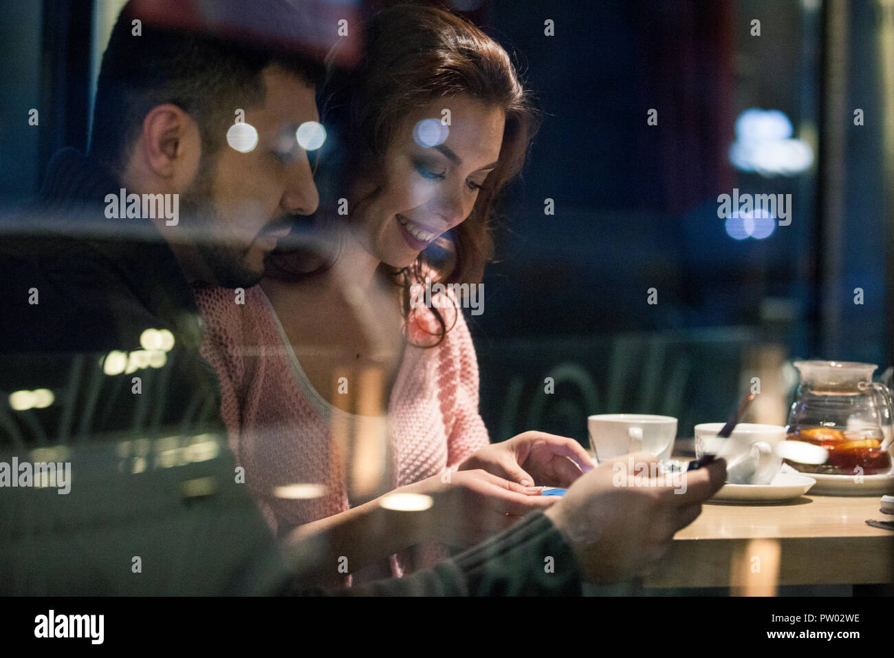 Paar durch ein Fenster auf lokaler Kaffee Platz und genießen winter nacht mit heißen Getränken und beiläufiges Gespräch. Von außen durch den Wind geschossen Stockfoto