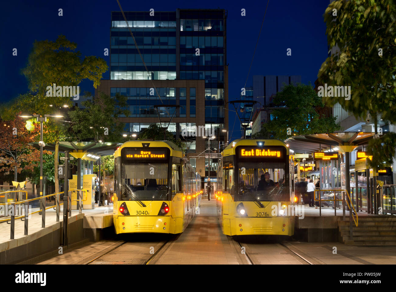 Zwei Metrolink Tram kommen am St. Peter's Square Stop in der Nacht im Stadtzentrum von Manchester, UK. Stockfoto