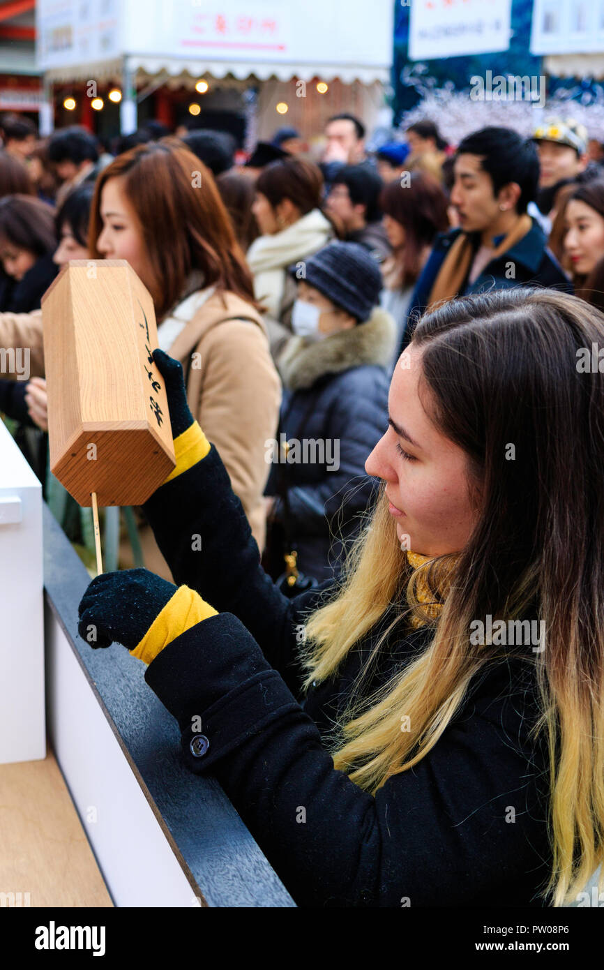 Japanische neues Jahr, shogatsu. Kaukasische junge Frau schütteln Omikuji Box das Papier fortune Slip in die ikuta Heiligtum in Kobe zu erhalten. Stockfoto