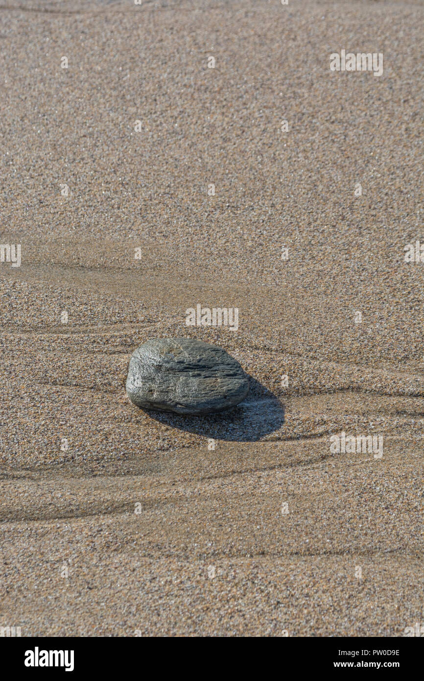 Isolierter Kieselstein auf nassem Strandsand. Für den letzten Mann stehend, ungeraden Mann heraus, Felsen ganz allein, einzelner Stein, verborgen vor dem Blick, Lassen Sie keinen Stein unverdreht. Stockfoto