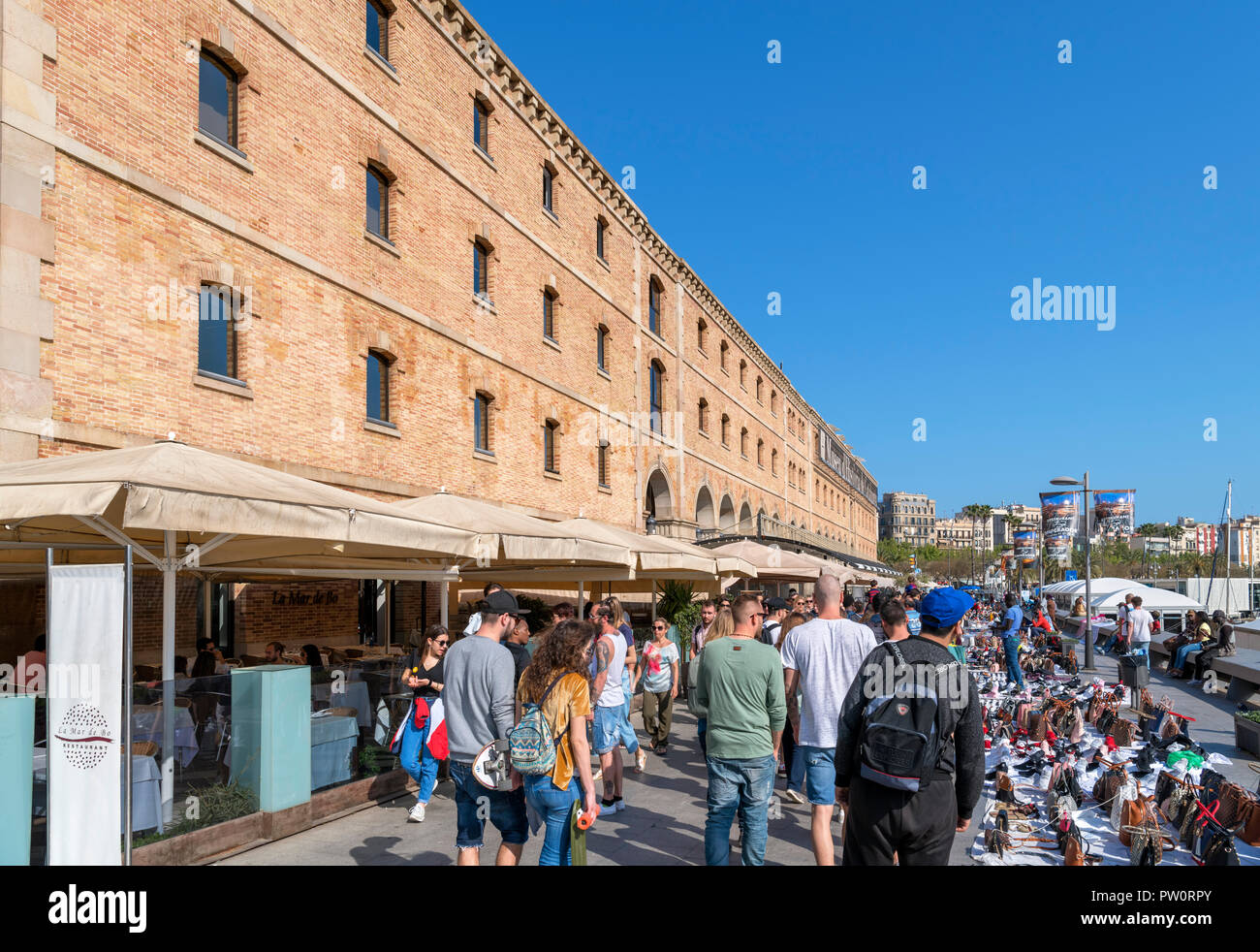 Straßenhändler und Touristen auf Moll del Dipòsit im Port Vell (Alter Hafen) mit dem Museu d'Història de Catalunya, Barcelona, Spanien Stockfoto