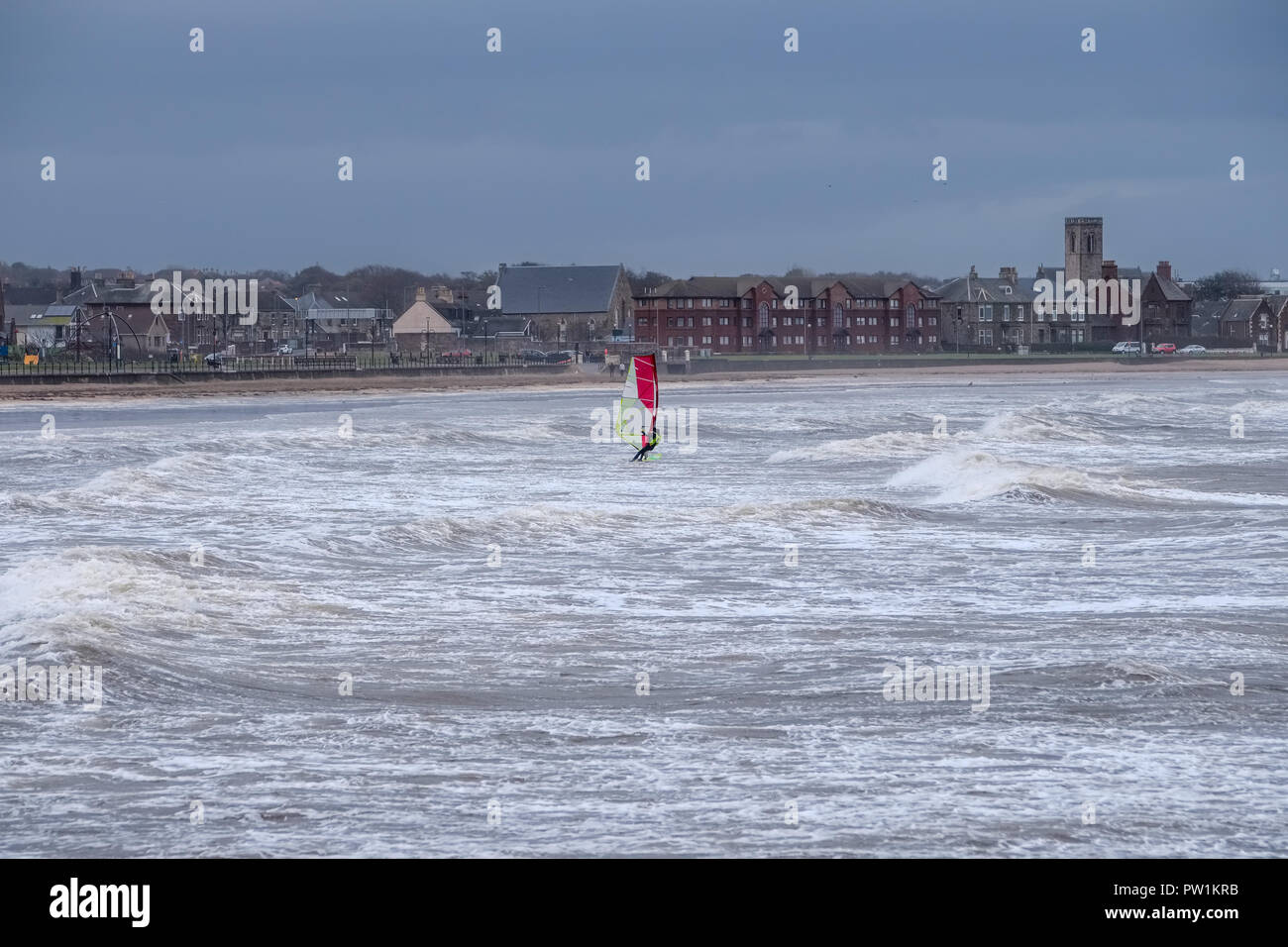 Stürmisches Wetter über Saltcoats Bay in Schottland, wie die Wellen pound den Hafen einer einzigen Windsurfer nutzt die dunstige Sturm Stockfoto