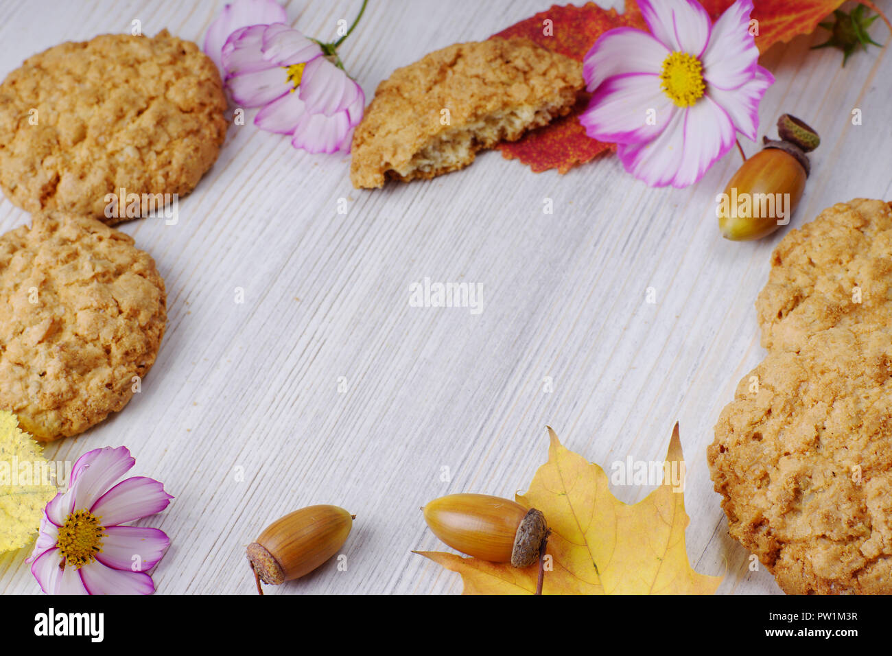 Abgefallene Blätter von roten und gelben Blumen, die entlang der Kanten zusammen mit Cookies und Blumen verteilt. Rahmen für Text über Herbst. Essen Konzept. Stockfoto