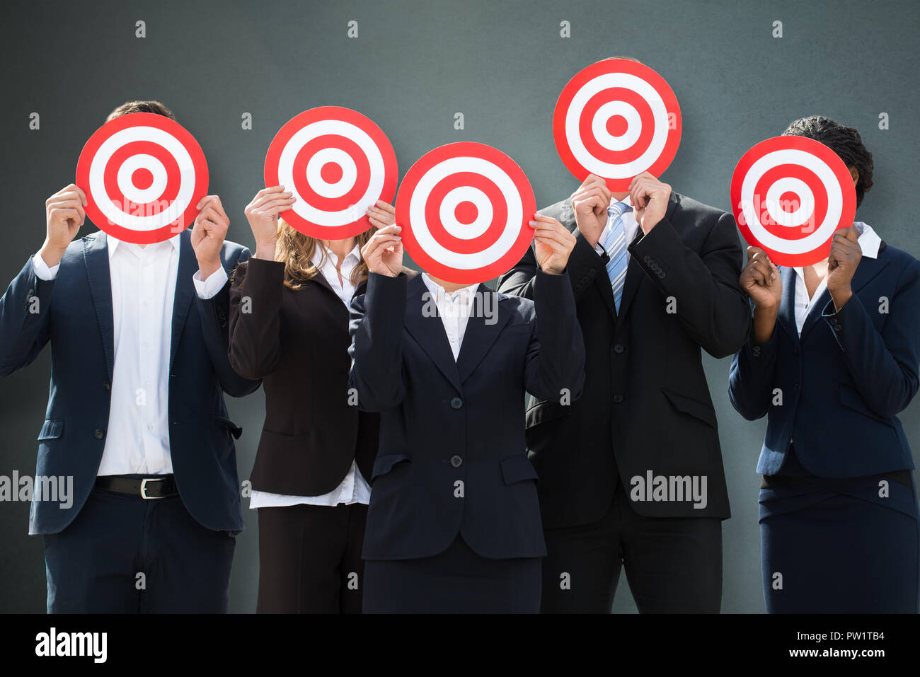 Gruppe von Geschäftsleuten verbergen ihre Gesichter hinter Dartscheibe auf grauem Hintergrund Stockfoto