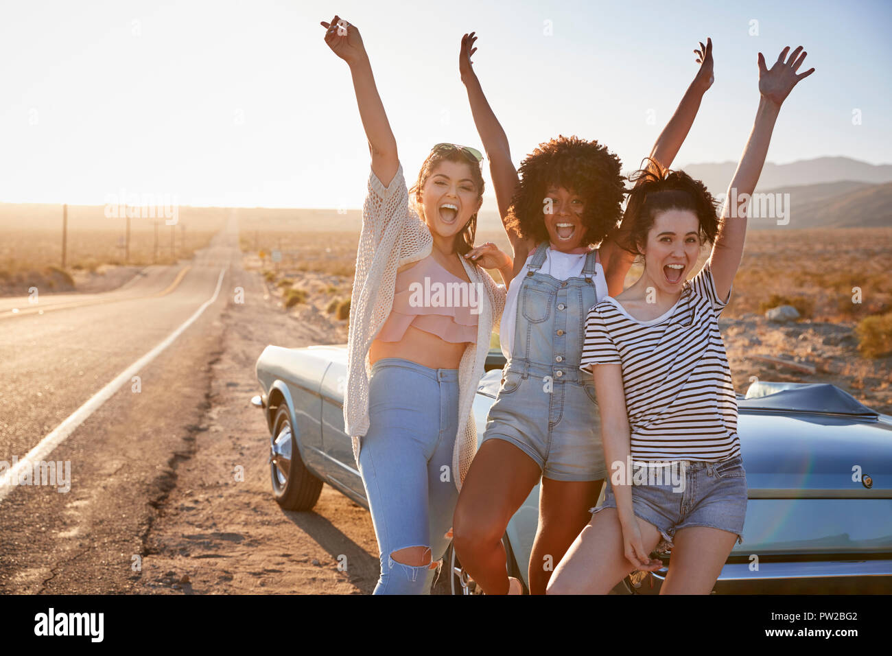 Portrait von weiblichen Freunde genießen Reise stehen Neben klassischen Auto auf dem Desert Highway Stockfoto