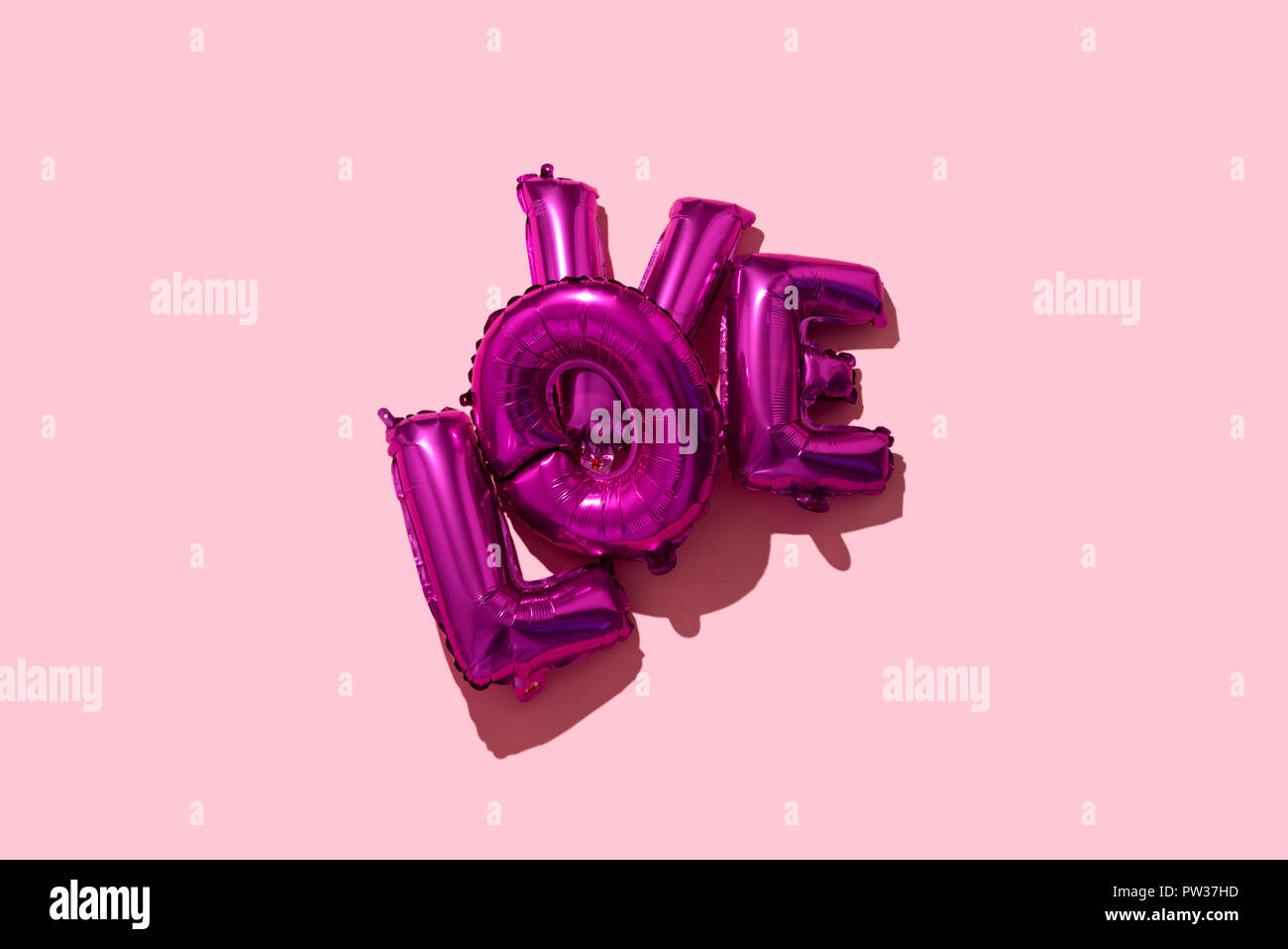 Einige fuchsia Brief-förmige Ballons, die wor Liebe auf einem rosa Hintergrund, mit einigen leeren Raum um Sie herum Stockfoto