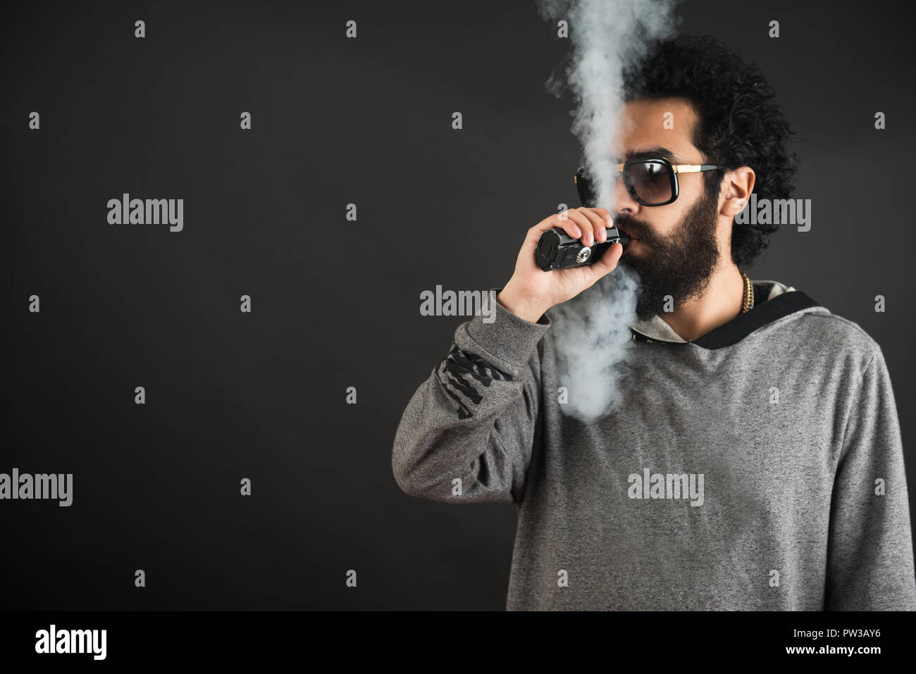 Vaping Mann hält ein Mod. Eine Wolke von Dampf. Schwarzen Hintergrund. Vaping eine elektronische Zigarette mit viel Rauch. Vape Konzept Stockfoto