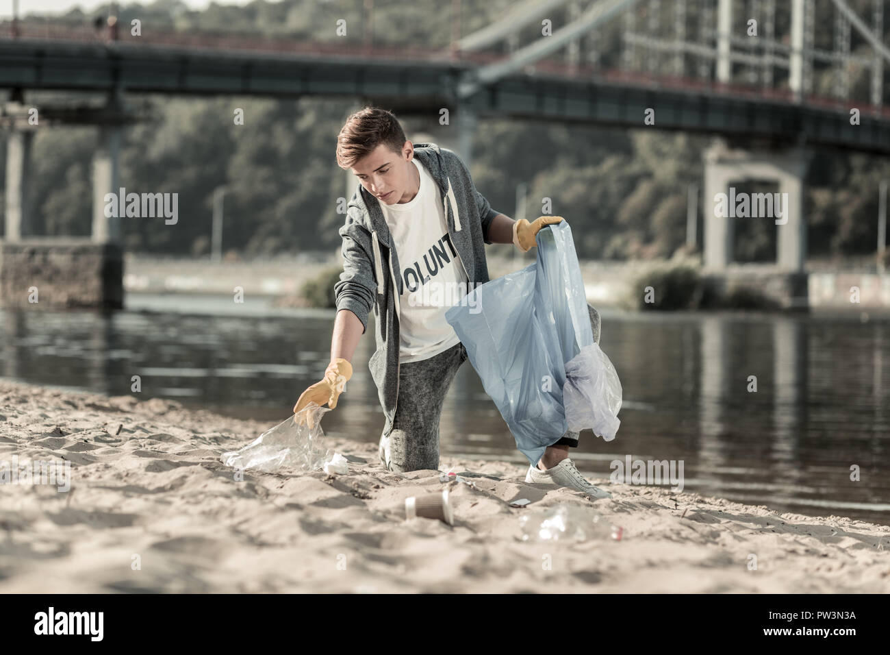 Junge dunkelhaarige Freiwilligen, der sein Tag Reinigung der Sand am Strand Stockfoto
