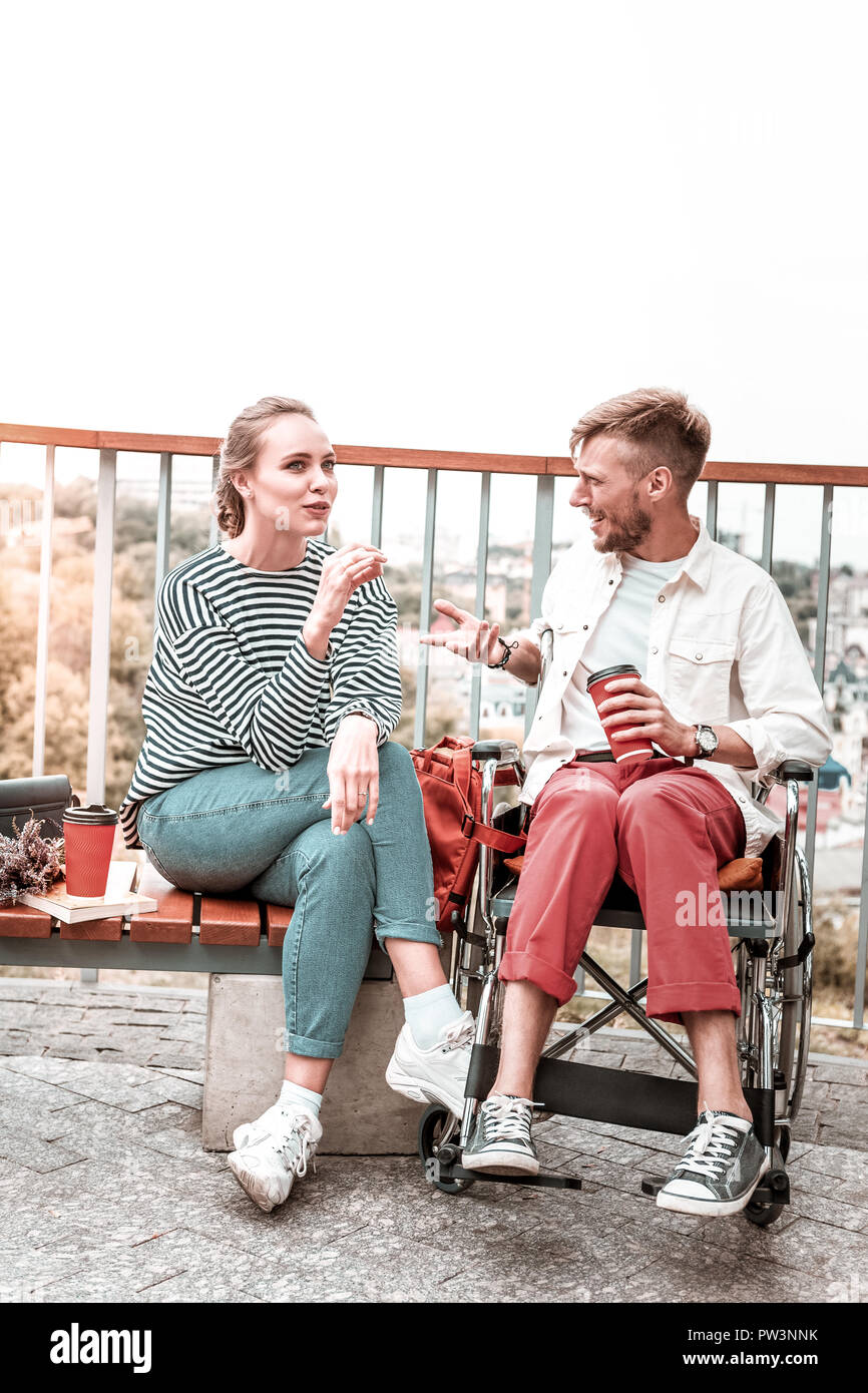 Mann sitzt im Rollstuhl und mit Blick auf seine neugierigen Freund beim Sprechen Stockfoto