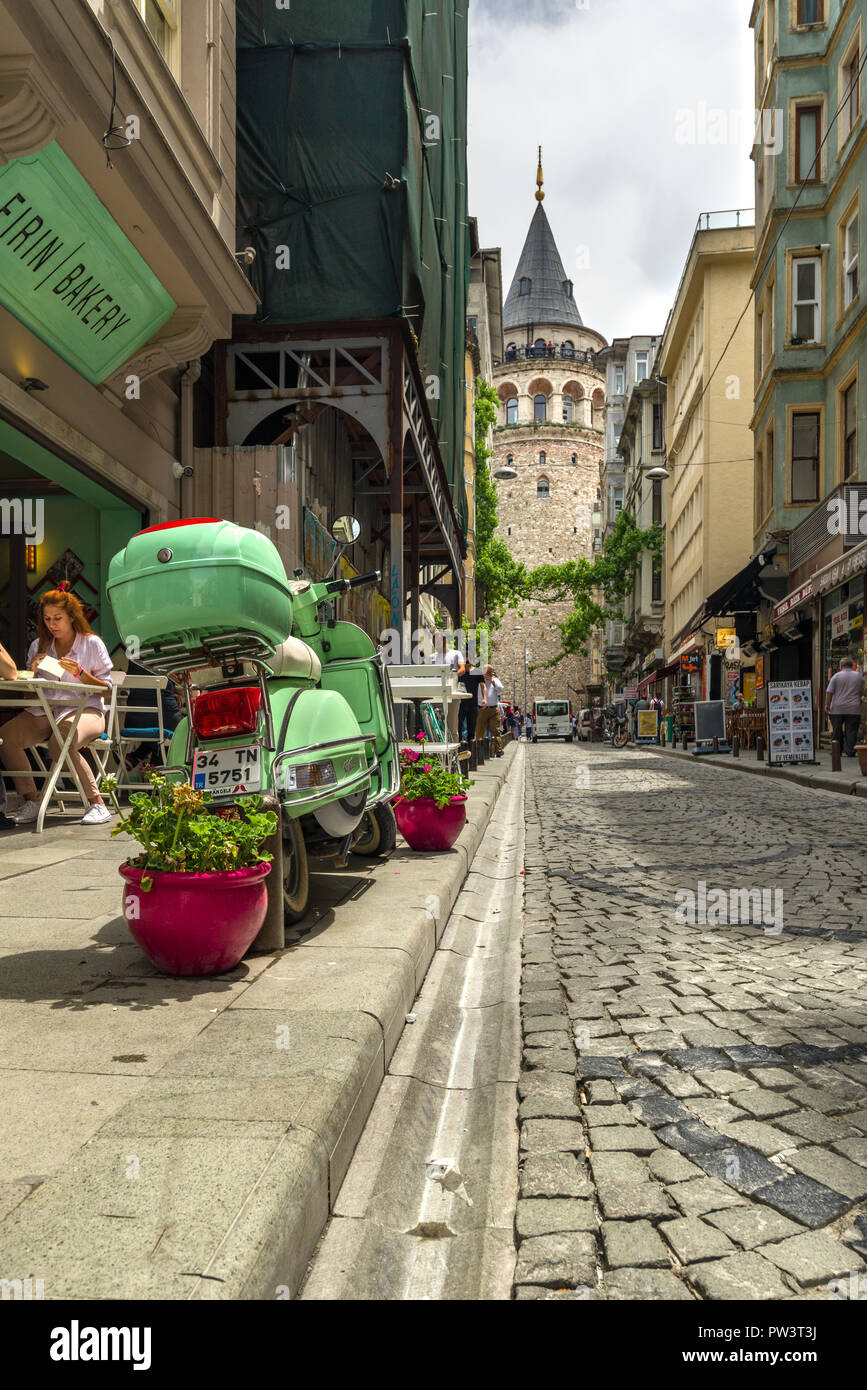 Galata Turm dominiert die Skyline als Menschen außerhalb in einem Cafe mit einem hellen Grün Moped in der Nähe geparkt, Istanbul, Türkei sitzen Stockfoto