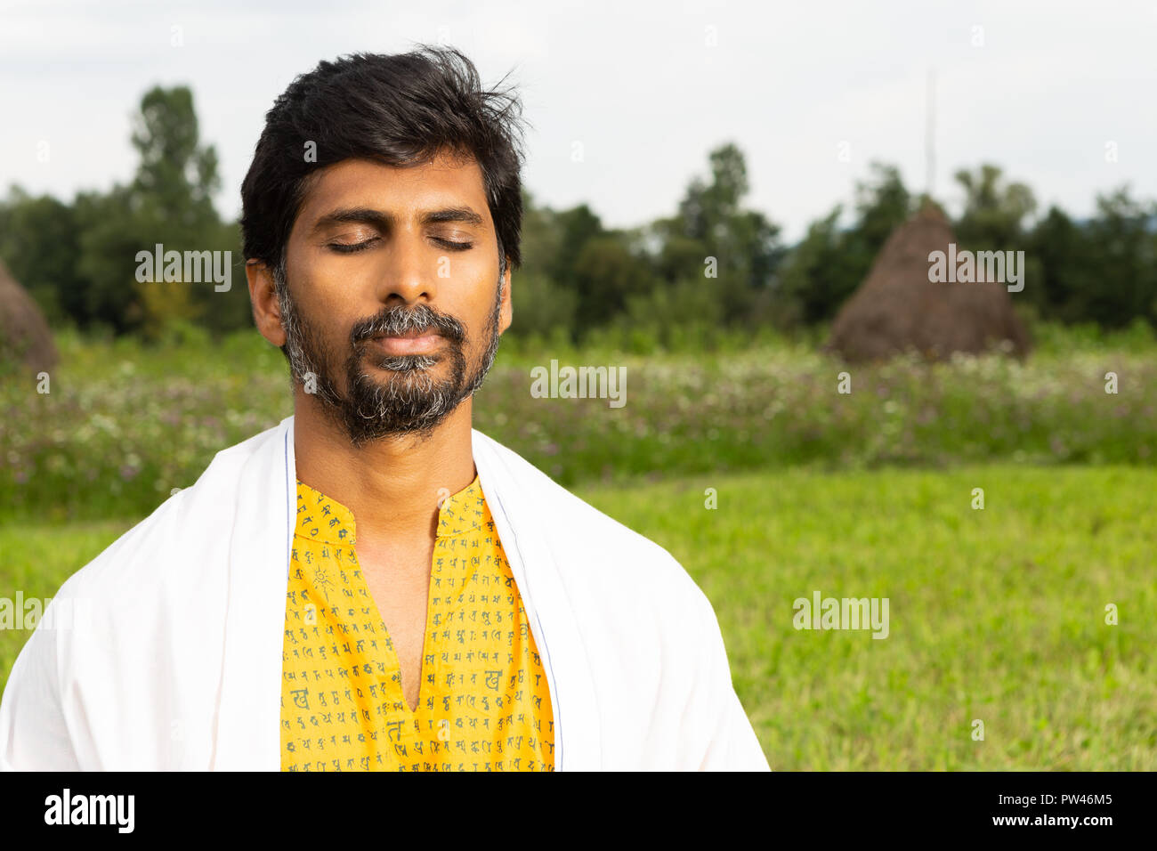 Indische männliche Person oder Yogi close-up der Ruhe Ausdruck mit geschlossenen Augen das Tragen von Weiß über Gelb Shirt mit natürlichen Hintergrund Stockfoto