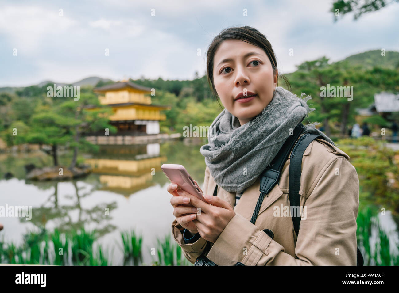 Elegante Frau, die in der Nähe des Teiches ein Blick auf die anderen, mit Kinkakuji Tempel im Hintergrund. Junge weibliche Reisende im Urlaub in Japan. Stockfoto