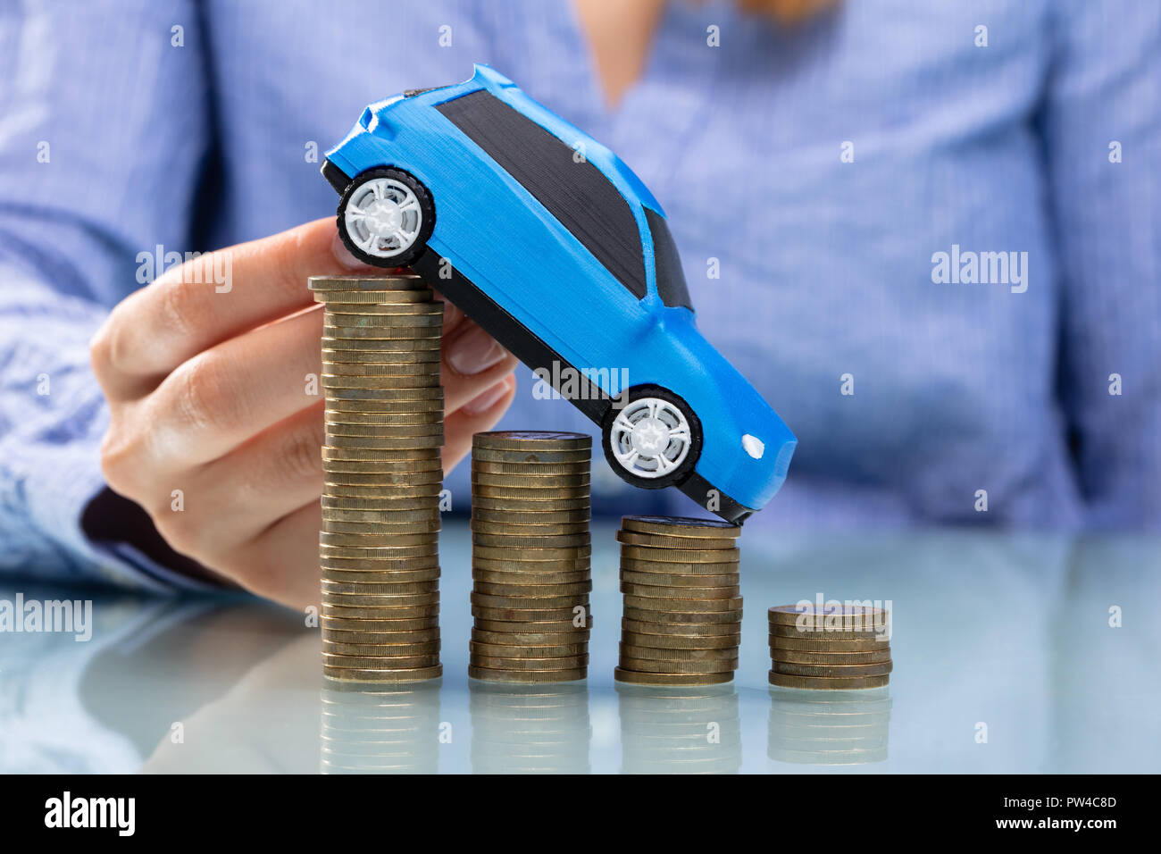 Die Geschäftsfrau Hand blau Auto auf sinkende Gestapelte Münzen über Schreibtisch Stockfoto