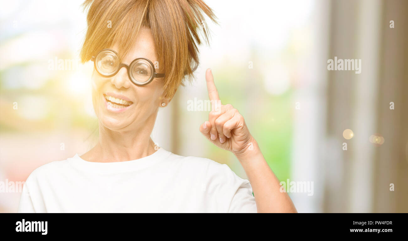 Crazy mittleren Alter Frau mit dummen Gläser heben Finger, die Nummer eins Stockfoto